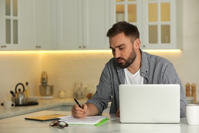 Photo of Young man working with laptop at home, space for text