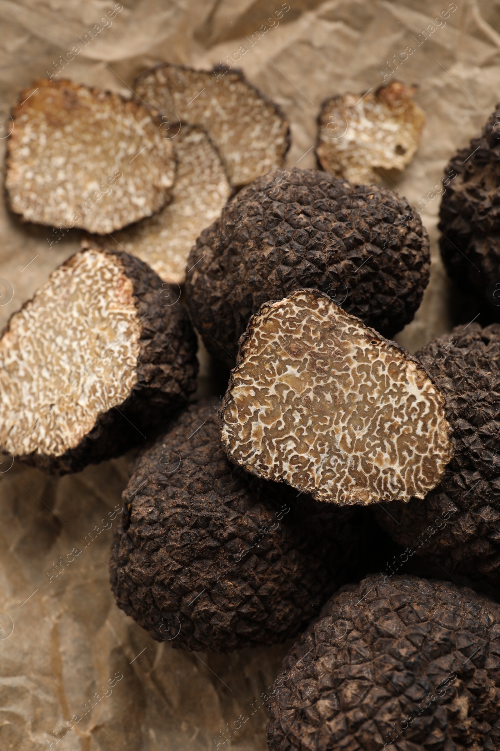 Photo of Whole and cut black truffles on parchment, closeup