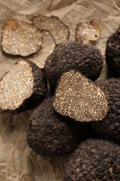 Photo of Whole and cut black truffles on parchment, closeup