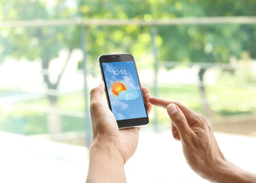 Image of Man using weather forecast app on smartphone near window, closeup