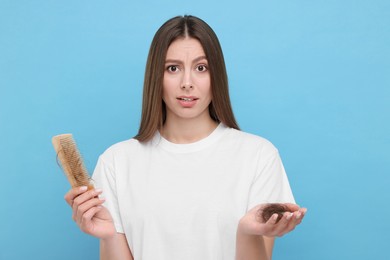 Photo of Emotional woman holding comb with lost hair on light blue background. Alopecia problem