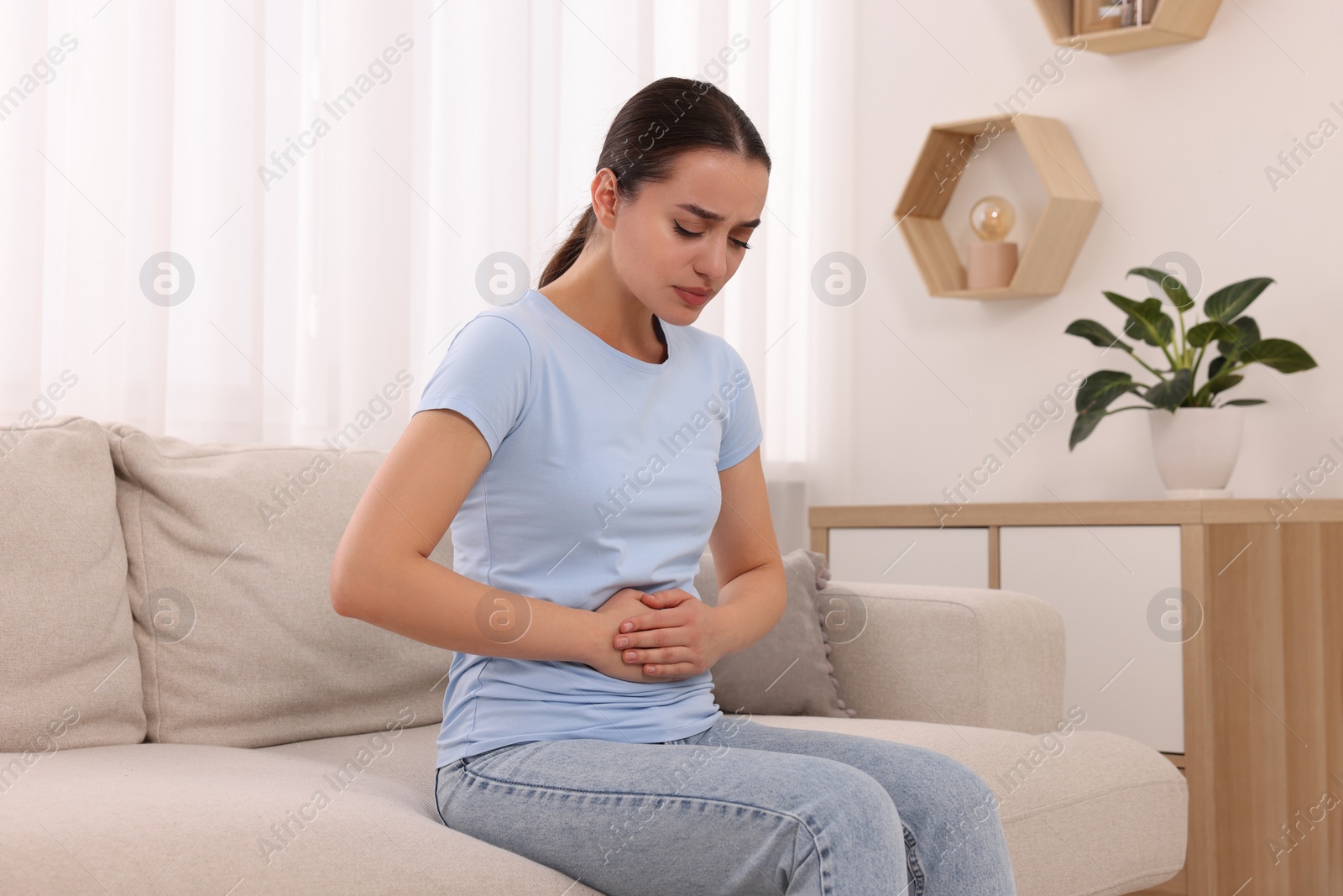 Photo of Woman suffering from abdominal pain on sofa at home. Unhealthy stomach