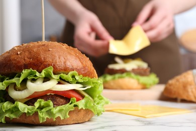 Photo of Woman making delicious vegetarian burger at white marble table, selective focus