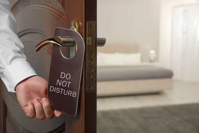 Image of Man putting hanger on hotel door handle indoors, closeup