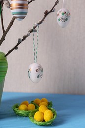 Photo of Beautiful willow branches with painted eggs and Easter decor on light blue table