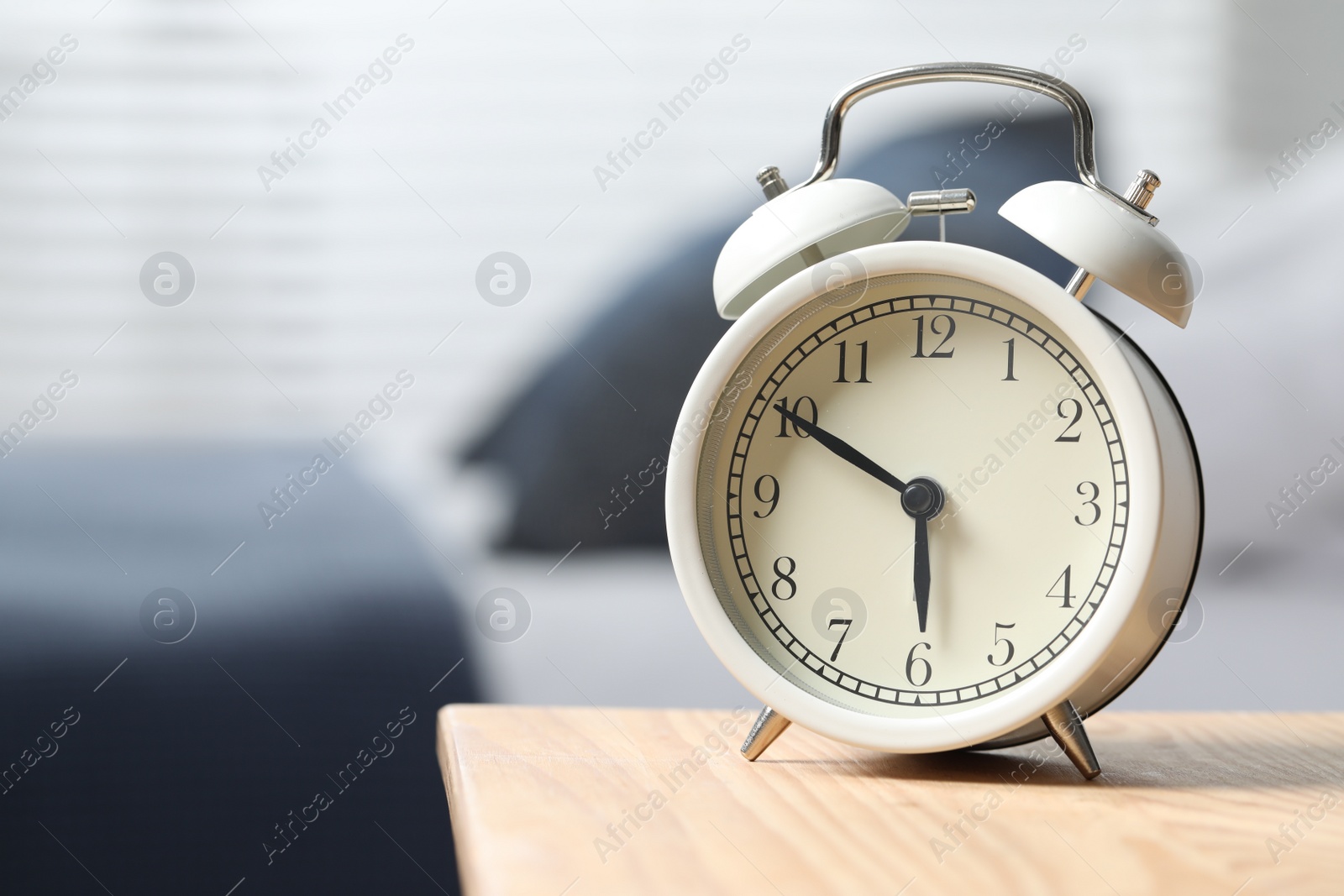 Photo of White alarm clock on wooden nightstand in bedroom, space for text