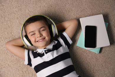Photo of Cute little boy listening to audiobook on floor, top view