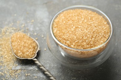 Photo of Brown sugar in bowl and spoon on grey textured table, closeup