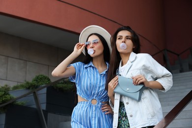 Stylish women blowing gums near beautiful building outdoors