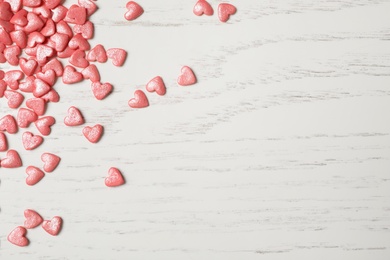 Photo of Pink heart shaped sprinkles on white wooden table, flat lay. Space for text