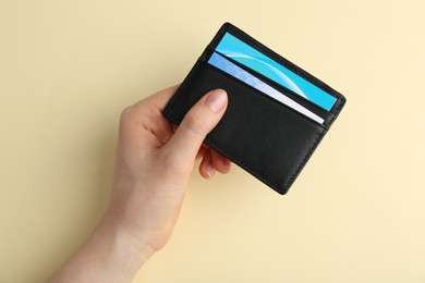 Photo of Woman holding business card holder with colorful cards on light yellow background, top view