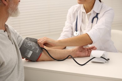 Nurse measuring elderly patient's blood pressure at white table in hospital, closeup
