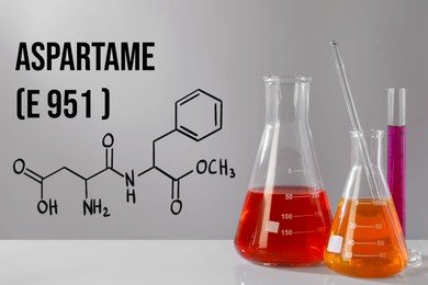 Image of Chemical structural formula of aspartame (E951) and laboratory glassware with liquids on gray table