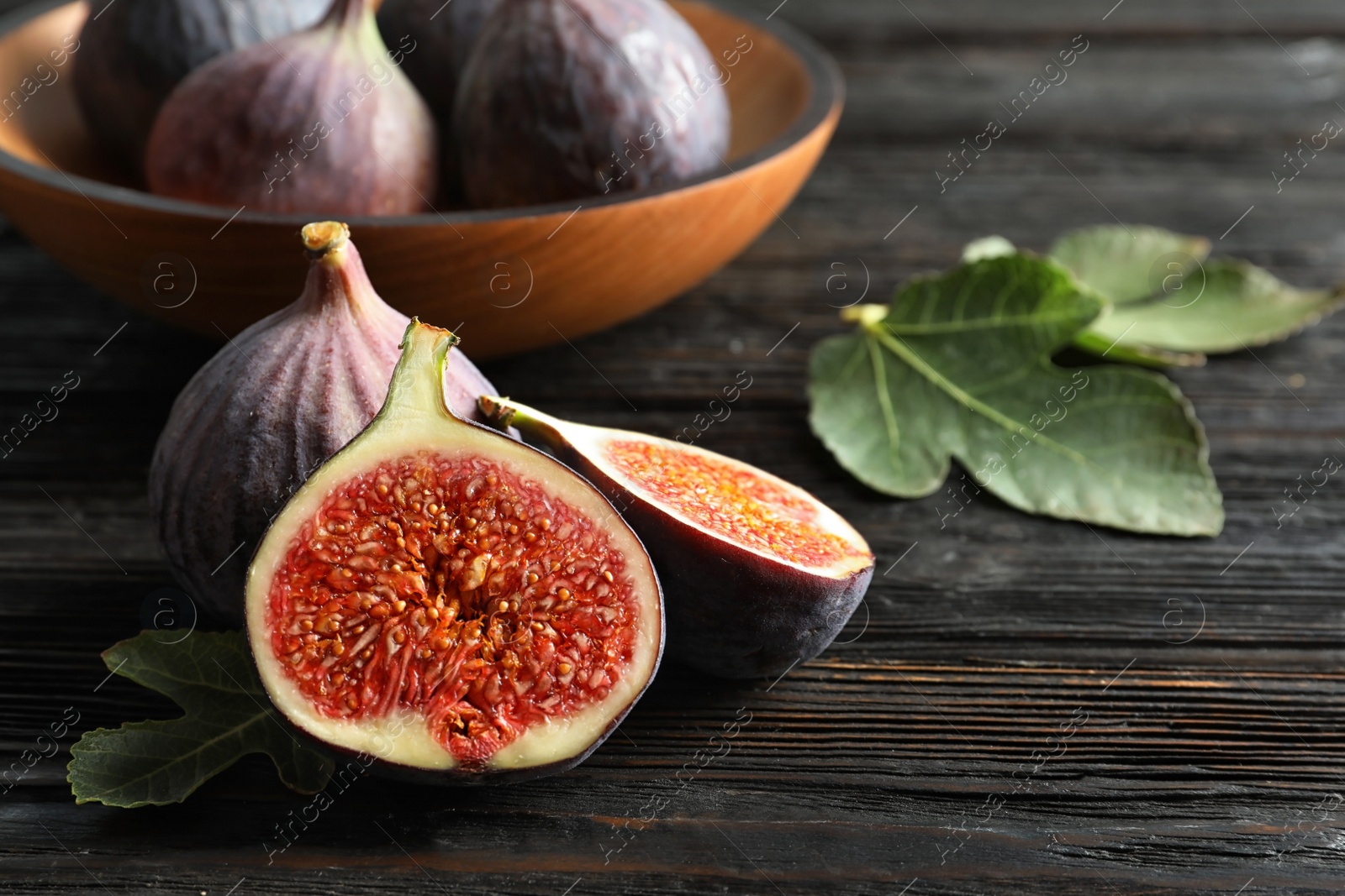 Photo of Fresh ripe figs with leaves on wooden table. Tropical fruit