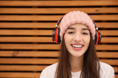 Photo of Young woman listening to music with headphones against wooden wall. Space for text