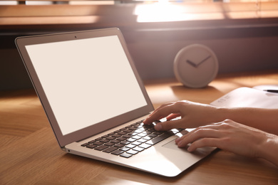 Photo of Woman using modern laptop at wooden table indoors, closeup