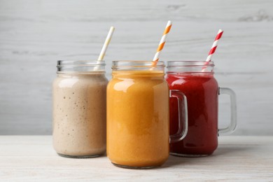 Photo of Mason jars with different tasty smoothies on white wooden table