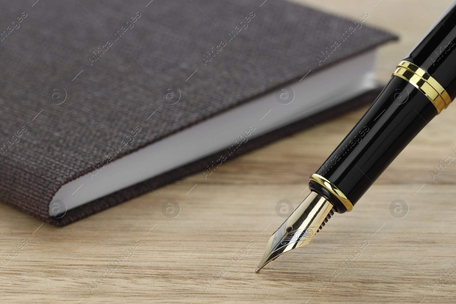 Photo of Stylish fountain pen and notebook on wooden table, closeup