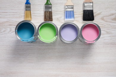 Photo of Cans of pastel paints and brushes on white wooden table, flat lay. Space for text