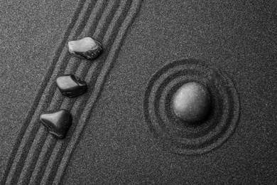 Photo of Black sand with stones and beautiful pattern, flat lay. Zen concept