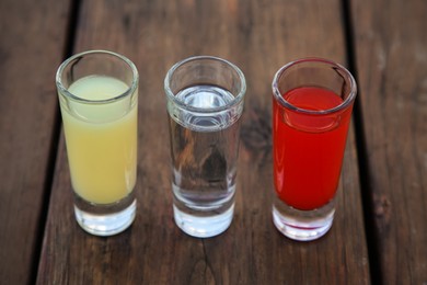Shots with lime juice, tequila and sangria as colors of mexican flag on wooden table, closeup. Traditional serving