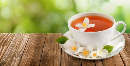 Image of Cup of jasmine tea and fresh flowers on wooden table outdoors, space for text. Banner design