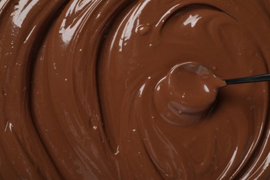 Spoon with tasty milk chocolate paste as background, top view