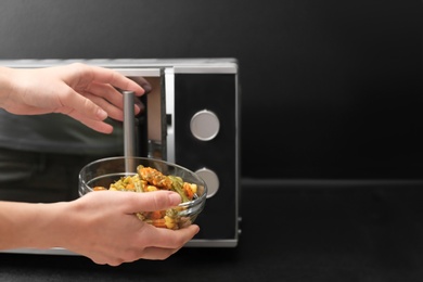 Young woman using microwave oven on table in kitchen, space for text