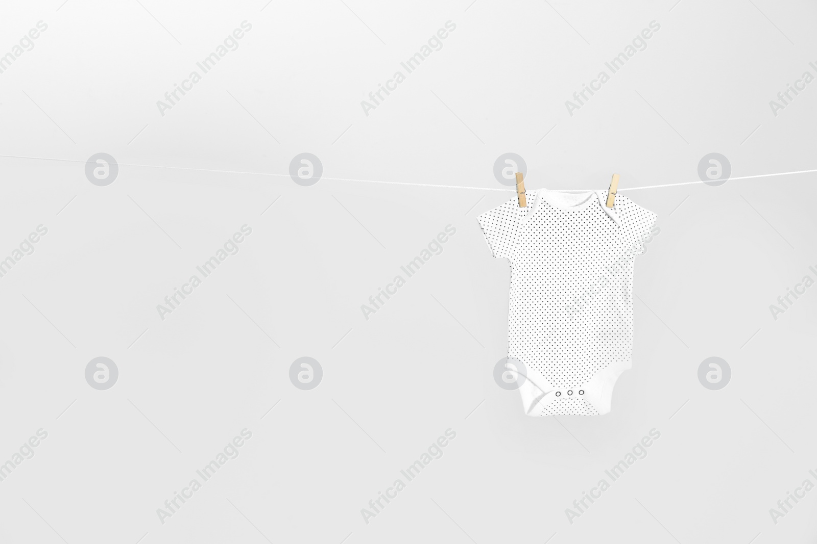 Photo of Cute baby onesie hanging on clothes line against light grey background, space for text. Laundry day