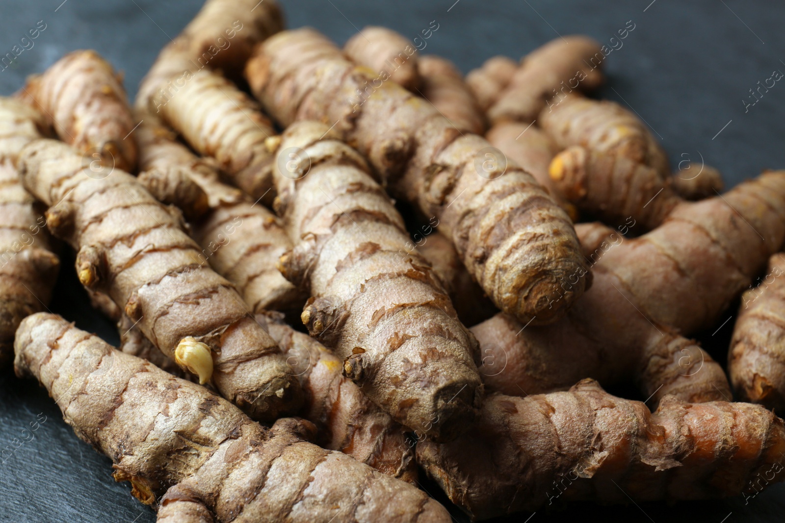 Photo of Many raw turmeric roots on black textured table, closeup