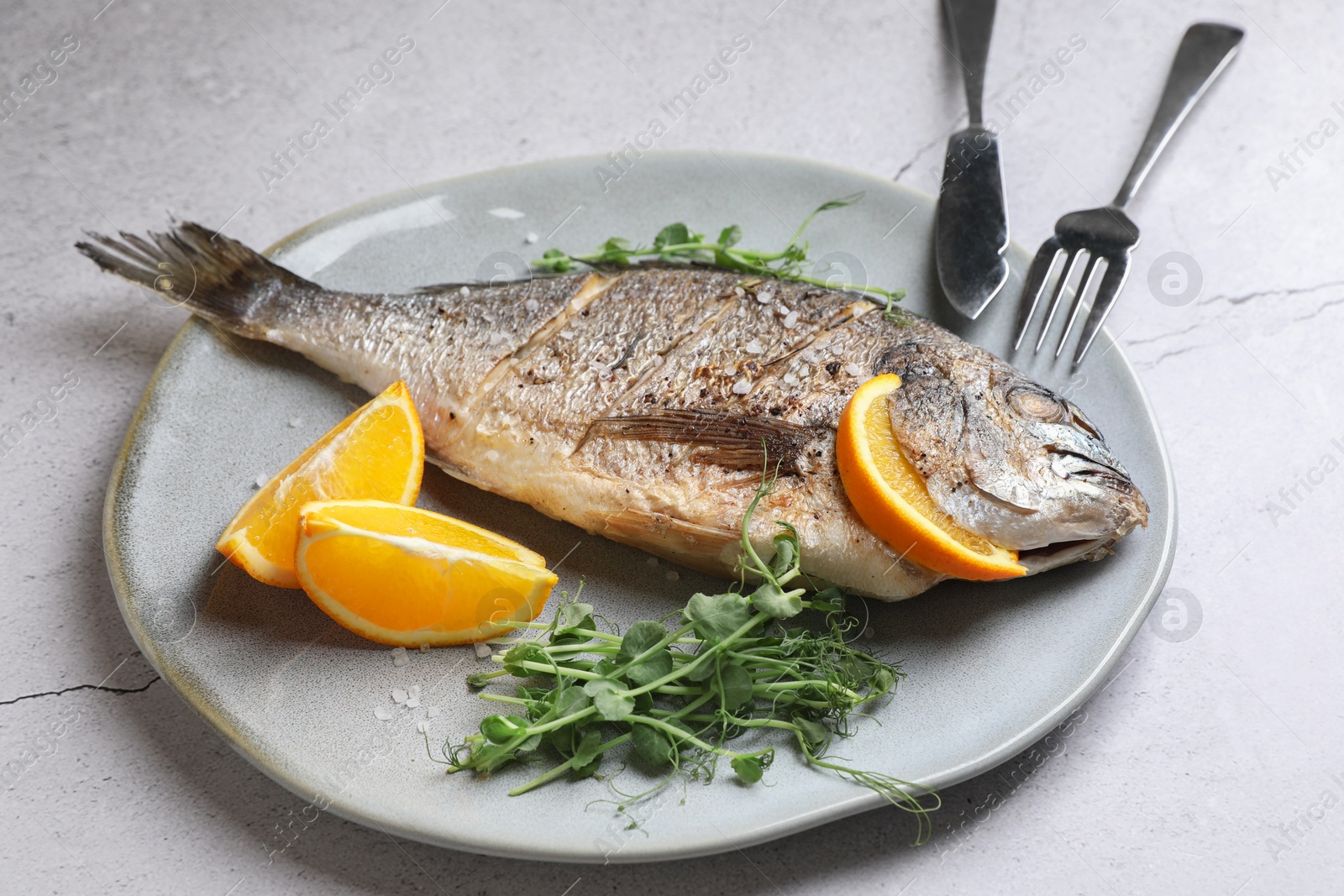 Photo of Seafood. Delicious baked fish served with orange and microgreens on light textured table, closeup