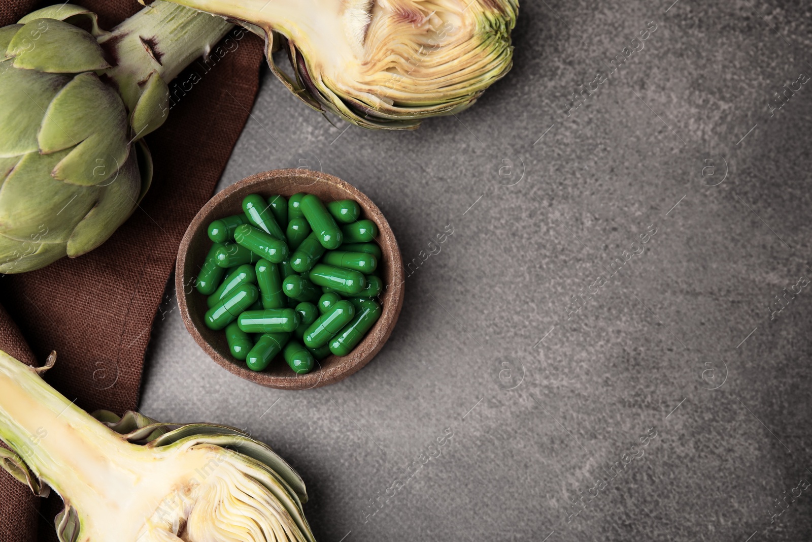 Photo of Bowl with pills and fresh artichokes on brown table, flat lay. Space for text