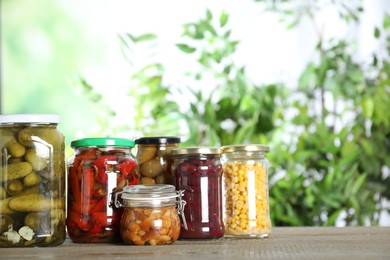 Photo of Glass jars of different pickled vegetables on wooden table