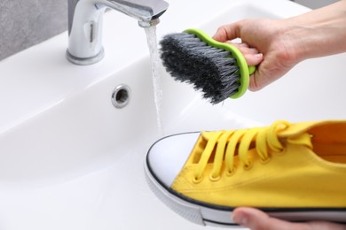 Photo of Woman washing stylish sneakers with brush in sink, closeup