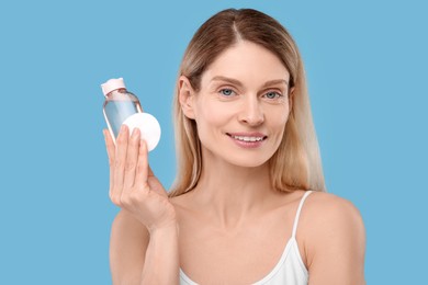Photo of Beautiful woman with makeup remover and cotton pad on light blue background