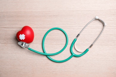 Photo of Stethoscope and red heart with adhesive plasters on wooden background, top view. Cardiology concept