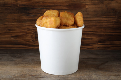 Photo of Bucket with tasty chicken nuggets on wooden table
