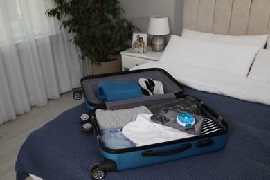 Photo of Open suitcase with packed clothes, accessories and pill box on bed indoors