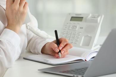 Photo of Assistant with telephone handset writing at white table in office, closeup