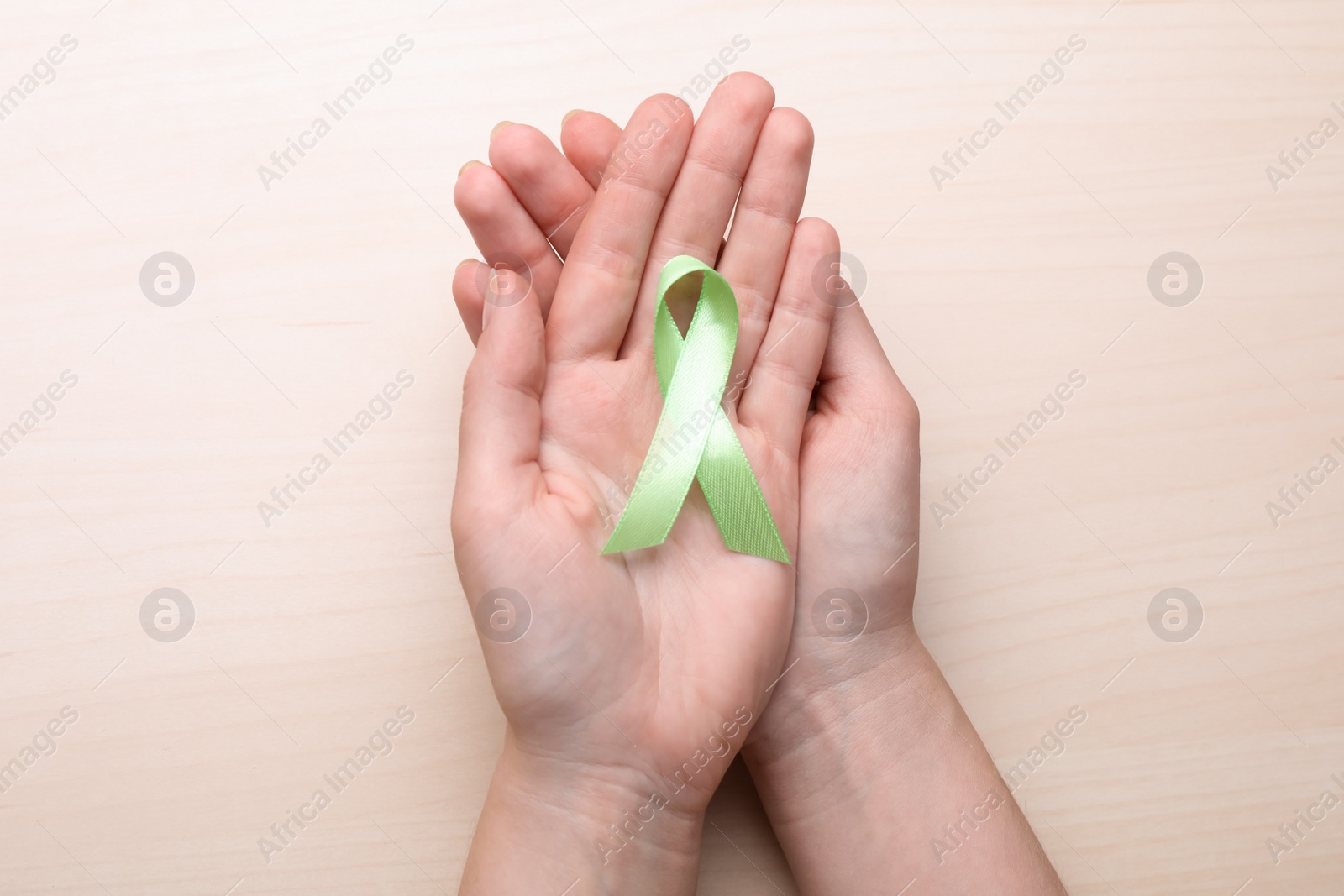 Photo of World Mental Health Day. Woman holding green ribbon on wooden background, top view