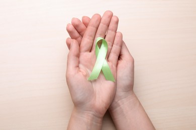Photo of World Mental Health Day. Woman holding green ribbon on wooden background, top view