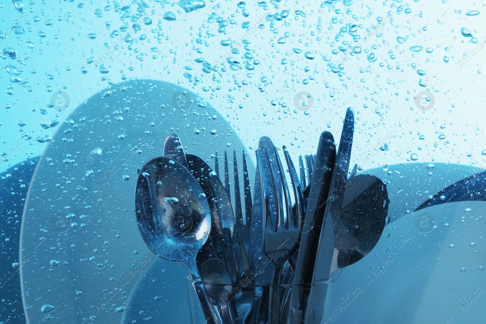 Photo of Washing silver cutlery and plates in water on light blue background