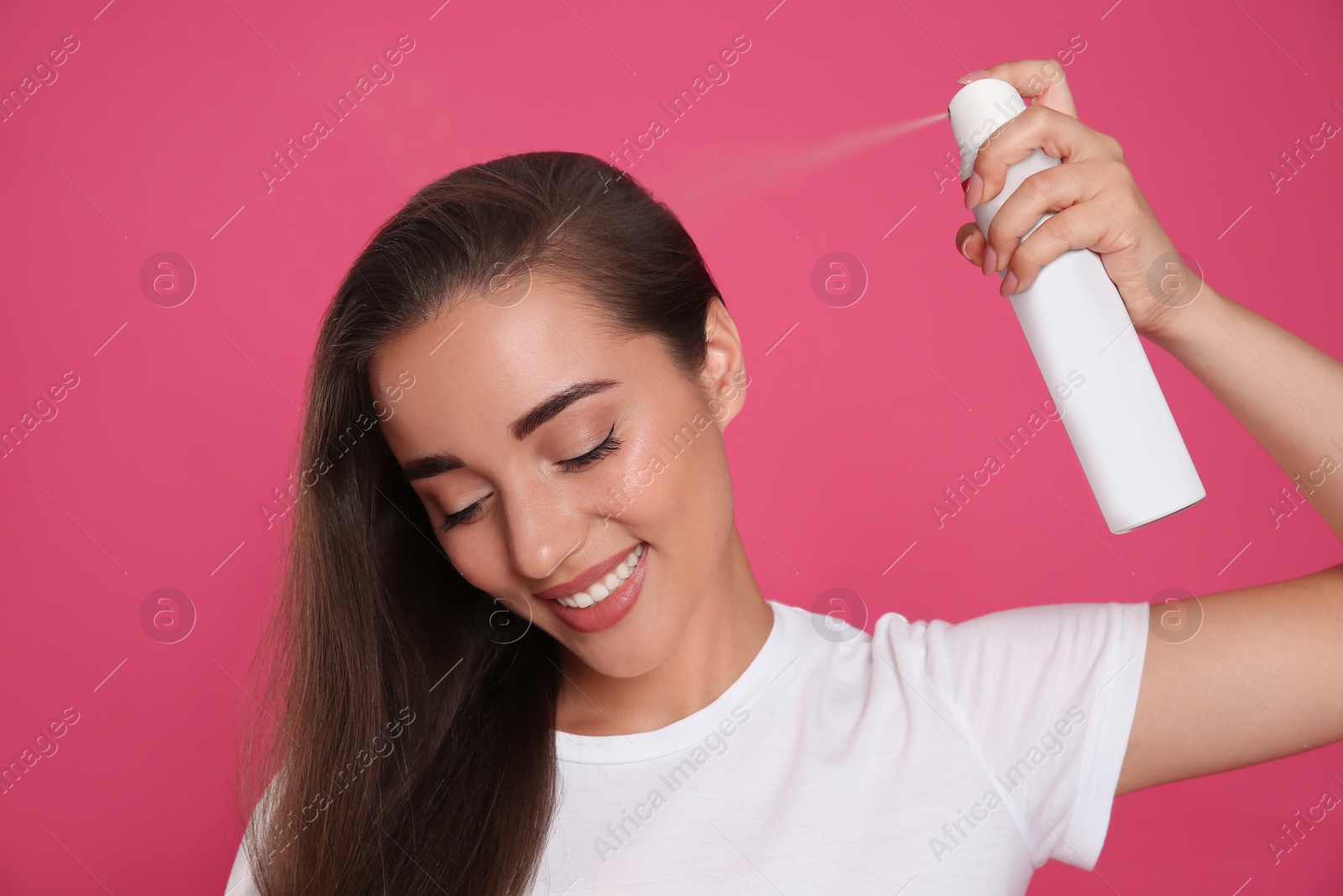 Young woman applying dry shampoo against pink background Photo of Young woman applying dry shampoo against pink background