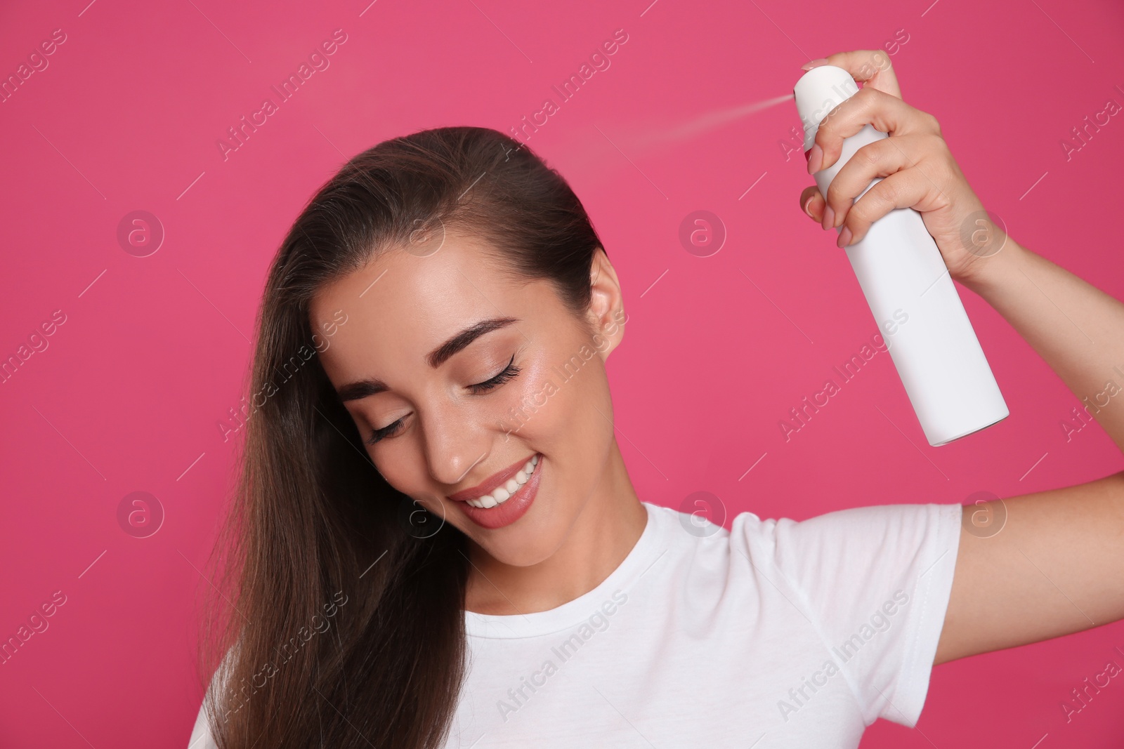 Photo of Young woman applying dry shampoo against pink background