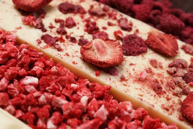 Photo of White chocolate bar with freeze dried strawberries as background, closeup