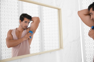 Photo of Handsome young man applying deodorant in bathroom