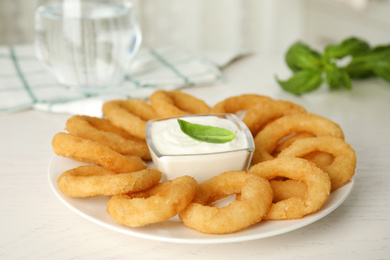 Photo of Delicious onion rings with sauce on white wooden table, closeup