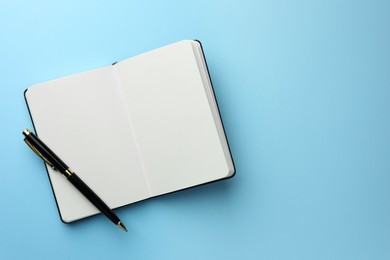 Photo of Open notebook with blank pages and pen on light blue background, top view. Space for text