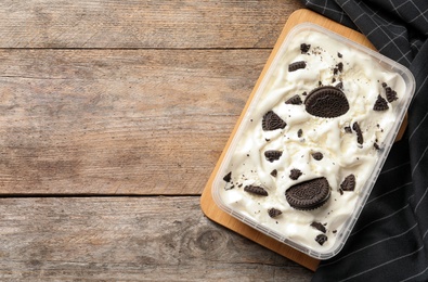 Photo of Container of ice cream with chocolate sandwich cookies on wooden background, top view. Space for text