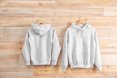 Photo of New hoodie sweaters with hangers on wooden wall. Mockup for design